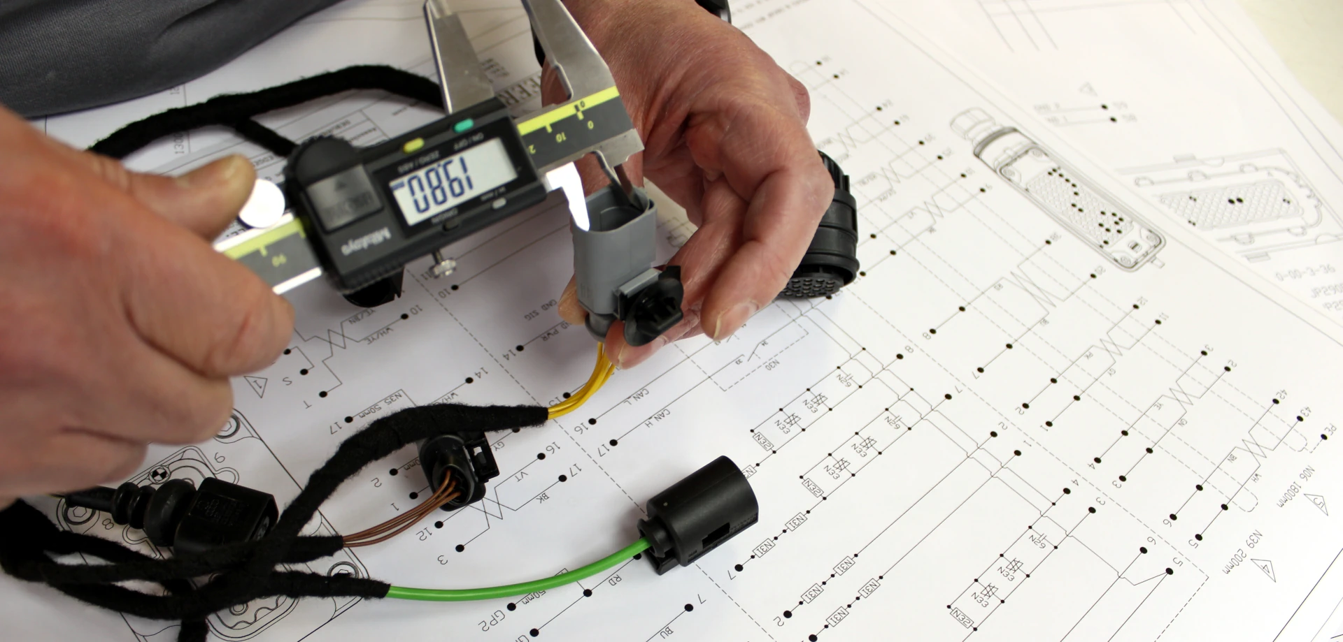 Grey connector being measured with calipers on a schematic background